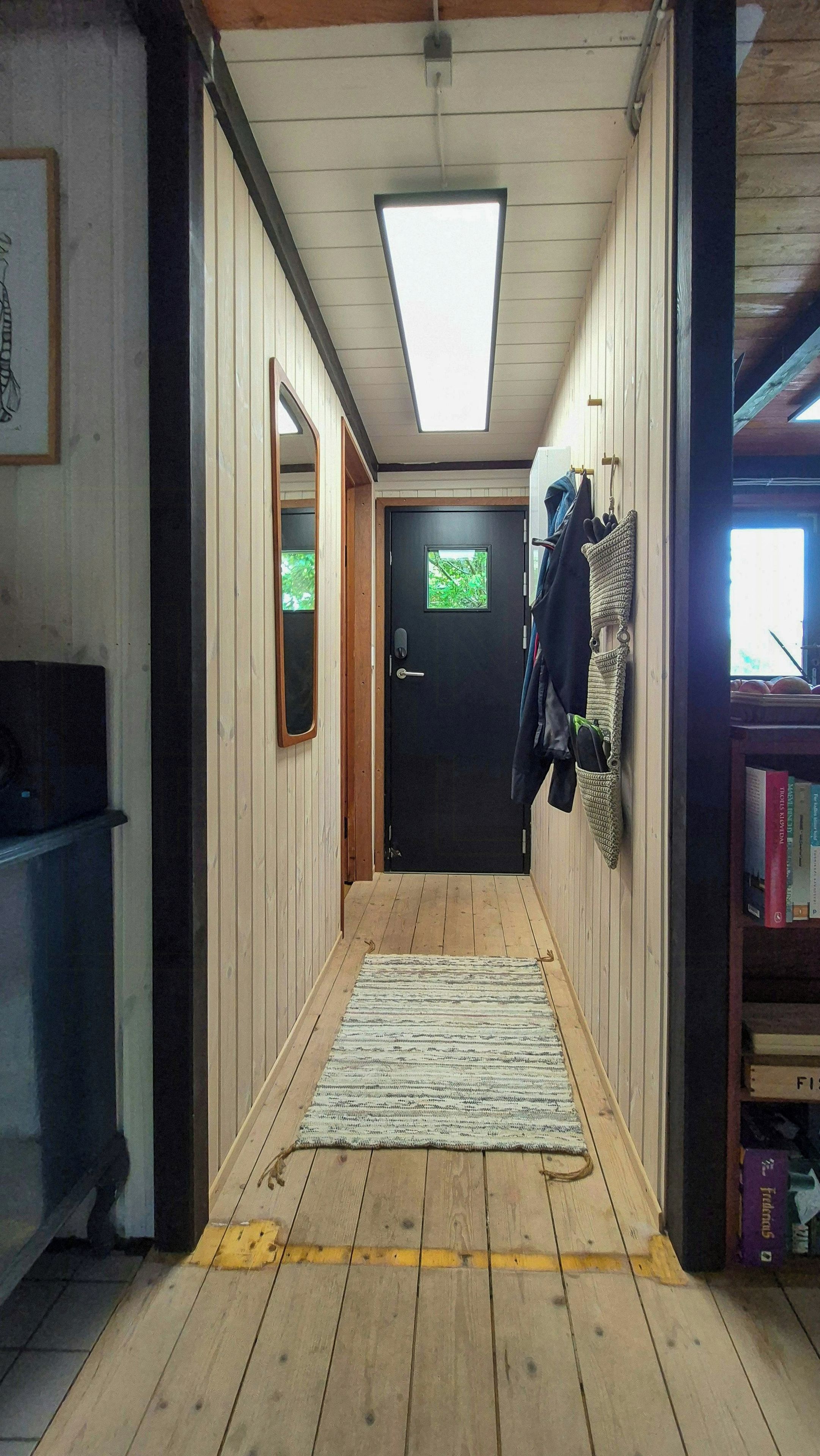 A narrow hallway with wooden walls, a black door at the end, a ceiling light, and a rug on the floor.