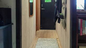 A narrow hallway with wooden walls, a black door at the end, a ceiling light, and a rug on the floor.