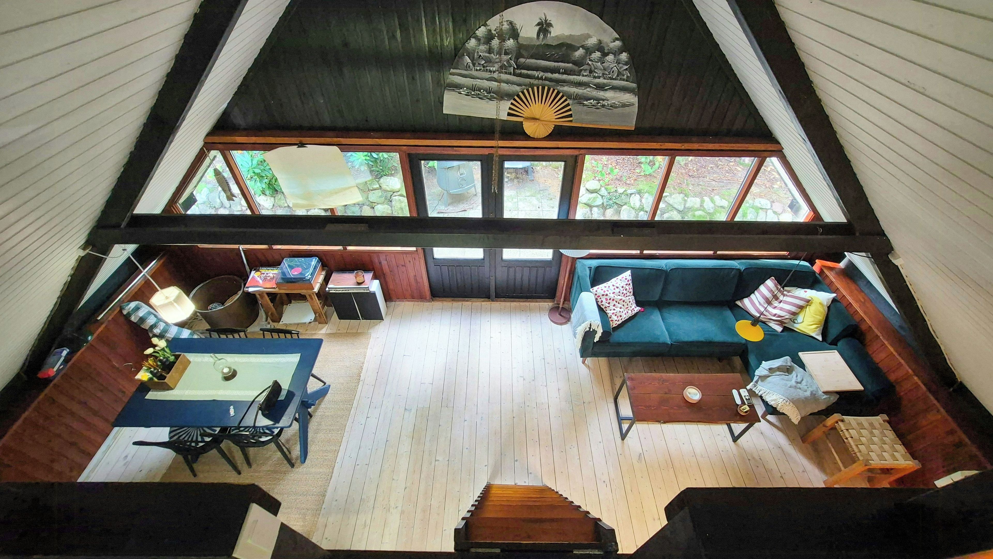 A high-ceilinged room with a large window, a sofa, a table, and a fan.