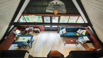 A high-ceilinged room with a large window, a sofa, a table, and a fan.
