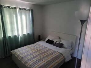 Ein Schlafzimmer mit Bett, Vorhängen, einem Nachttisch und einer Stehlampe.