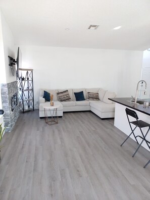 Ein modernes Wohnzimmer mit einem Ecksofa, einem Couchtisch und einer Küchenzeile mit Spüle und Barhocker.