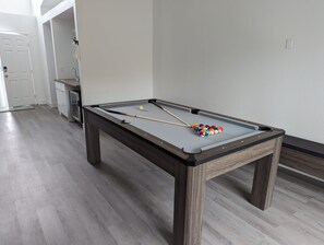 Ein Billardtisch in einem Raum mit Holzboden und einer weißen Tür im Hintergrund.