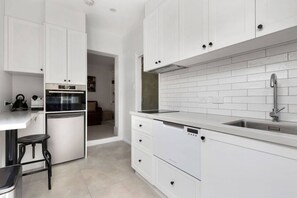 A modern kitchen with white cabinetry, a built-in oven, and a stainless steel sink. - Toris Cottages Near Waterfront Dining and Markets (Battery Point)
