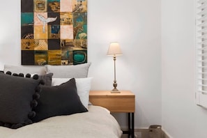 A bedroom with a bed, pillows, a bedside table with a lamp, and a wall art piece. - Toris Cottages Near Waterfront Dining and Markets (Battery Point)