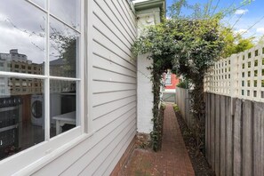 A narrow pathway leading to a wooden fence, with a window and washing machine visible in the background. - Toris Cottages Near Waterfront Dining and Markets (Battery Point)