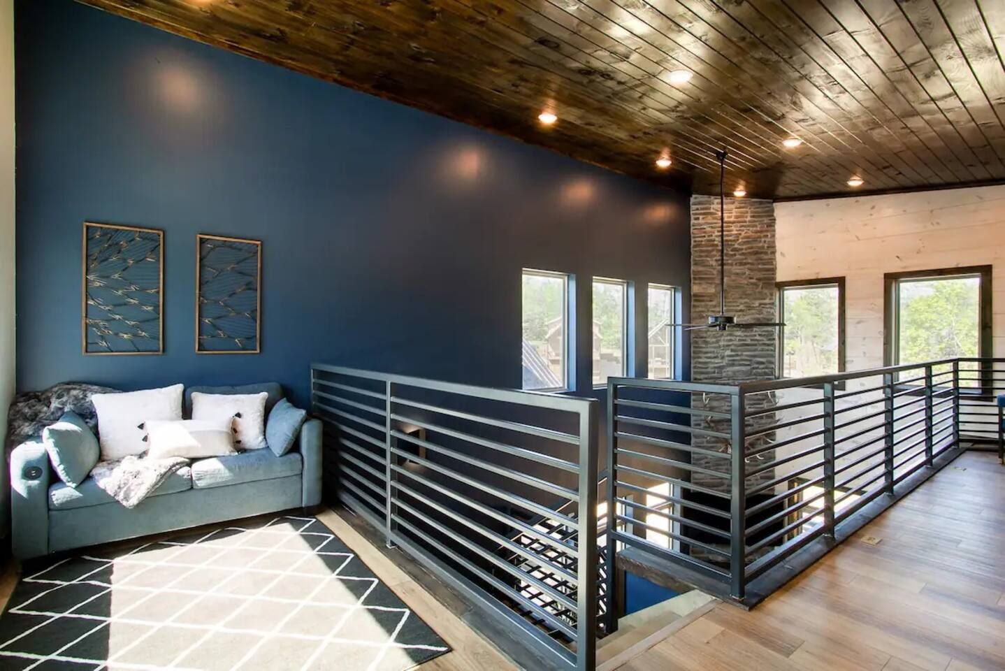 Un intérieur moderne avec un mur bleu, un canapé gris et une rambarde en métal.