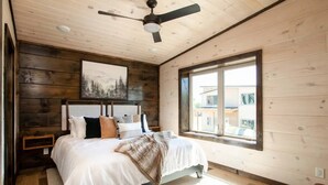 Une chambre à coucher avec un lit, un ventilateur de plafond, une fenêtre et un tableau accroché au mur.