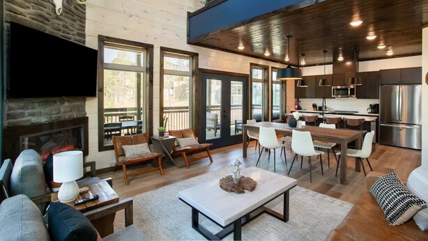 Un intérieur moderne avec une cheminée, un coin repas, une cuisine et une grande fenêtre donnant sur une terrasse.