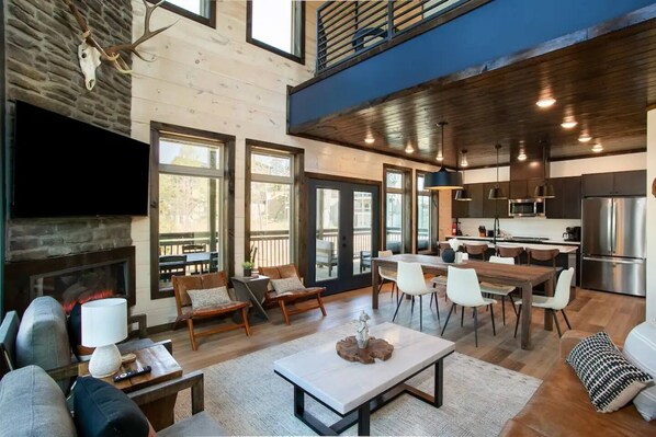 Interior moderno com lareira, área de refeições, cozinha e uma grande janela com vista para um deck.