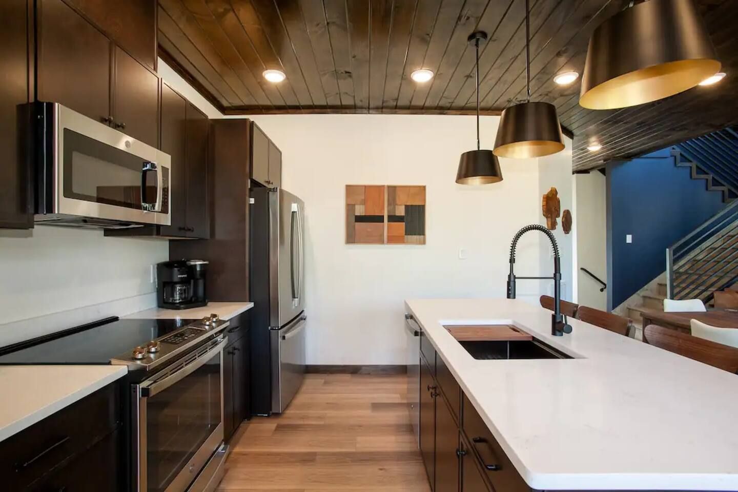 Une cuisine moderne dotée d’appareils électroménagers en acier inoxydable, d’un plafond en bois et de luminaires suspendus.