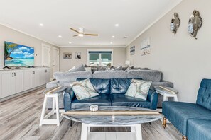 A modern living room with a blue leather sofa, a coffee table, and a TV. - Gorgeous Beachfront Luxury 6 BR Home | Elevator | Pet Friendly | Free Activities Including Free Golf (Oak Island)