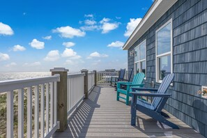 A wooden deck with chairs and a railing overlooking a beach. - Gorgeous Beachfront Luxury 6 BR Home | Elevator | Pet Friendly | Free Activities Including Free Golf (Oak Island)