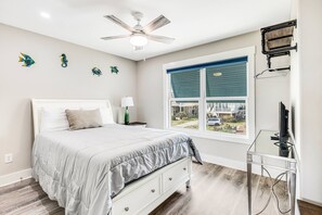 Et soveværelse med seng, ventilator, et vindue med persienner og et TV-bord.