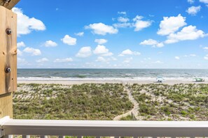 Blick auf einen Strand von einem Balkon mit Holzgeländer, feinem Sand und dem Meer.