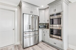A modern kitchen with stainless steel appliances, white cabinetry, and a wooden floor. - Gorgeous Beachfront Luxury 6 BR Home | Elevator | Pet Friendly | Free Activities Including Free Golf (Oak Island)