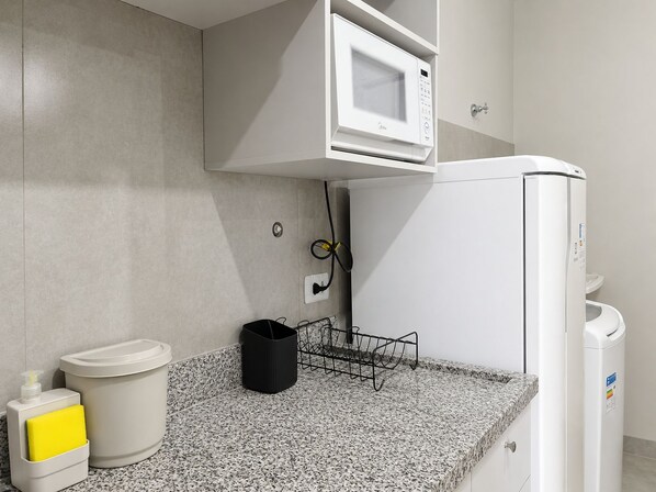 A modern kitchen with a built-in microwave, a water dispenser, and a trash bin.