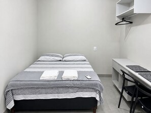 A small, neatly arranged bedroom with a bed, bedside table, and a chair.