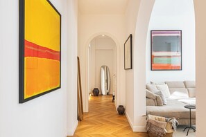 A hallway with a wooden floor, a framed abstract painting, a mirror, and a sofa with cushions. - Stunning Brand New 4BR 4BATH Center-Vatican (Rome)