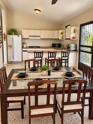 A modern kitchen with white cabinets, a dining table with chairs, and a view through a window. - Casa Carmín-3BR & Pet Friendly- San Sebastian (San Sebastián)