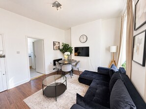 Ein modernes Wohnzimmer mit einem dunkelgrauen Sofa, einem Glastisch und einem Essbereich mit rundem Tisch und Stühlen.