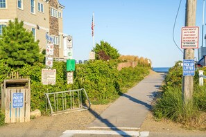 Un sentier menant à une plage, avec divers panneaux indiquant l’accès public, le règlement de la plage et l’absence de services municipaux sur la plage.