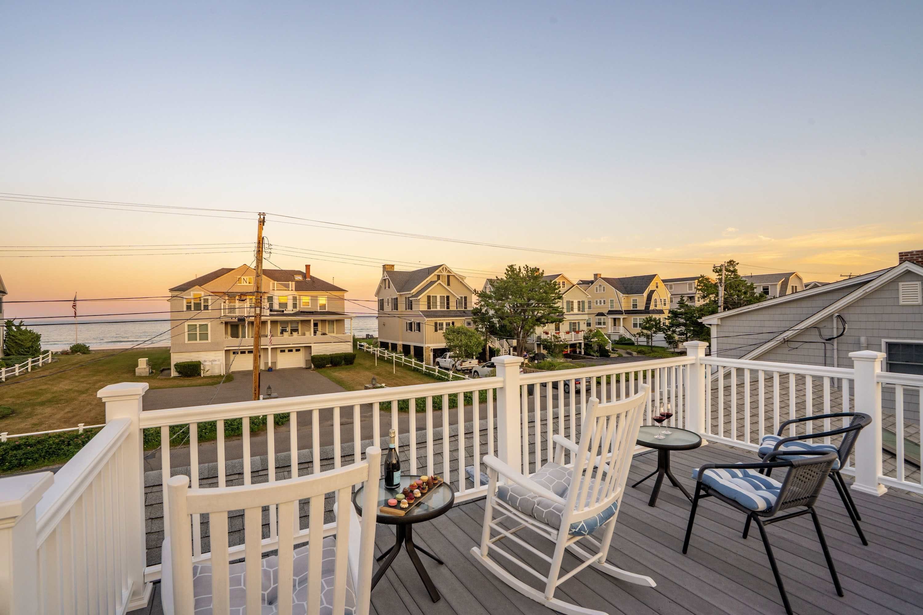 A deck with outdoor seating, overlooking a residential area with houses and a view of the ocean.