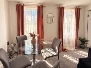 A room with a round glass table, four chairs, a vase with flowers, a fan, and a potted plant. - Stylish Fitzrovia 1BR Near Oxford Street (Greater London)