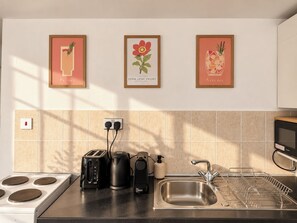 A kitchen with a stove, toaster, kettle, and sink. There are three framed pictures on the wall above the counter. - Stylish Fitzrovia 1BR Near Oxford Street (Greater London)