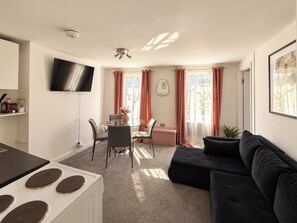 A modern living room with a sofa, a dining area with a table and chairs, a TV mounted on the wall, and a kitchen area with a stove. - Stylish Fitzrovia 1BR Near Oxford Street (Greater London)