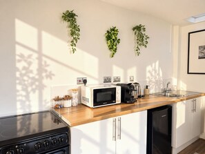 A modern kitchen with a microwave, toaster, and coffee maker on the counter, a stove, and a dishwasher. - Spacious Fitzrovia Studio Near Oxford Street (Greater London)