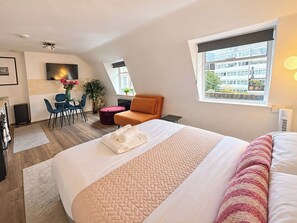 Ein modernes Hotelzimmer mit einem großen Bett, einem Schreibtisch mit Stuhl, einer Couch und einem Fenster mit Blick auf Gebäude.