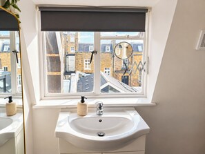 A bathroom with a white sink, a mirror, and a window with a view of buildings. - Spacious Fitzrovia Studio Near Oxford Street (Greater London)