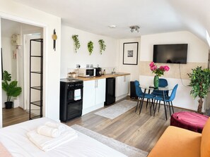 A modern kitchen with a microwave, stove, and cabinets, a dining area with a table and chairs, and a TV mounted on the wall. - Spacious Fitzrovia Studio Near Oxford Street (Greater London)