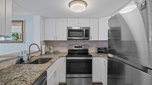 A modern kitchen with stainless steel appliances, white cabinets, a granite countertop, and a built-in oven. - Bright 2BR Beach Condo | Free Chairs + Attractions (St. Augustine)