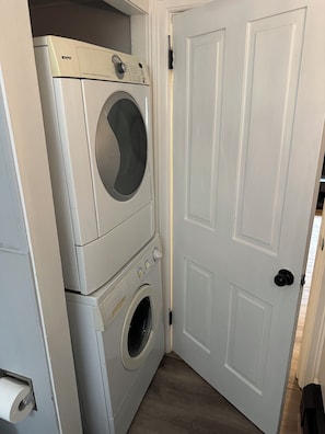 A laundry room with stacked washers and dryers, a door, and a visible toilet paper dispenser.