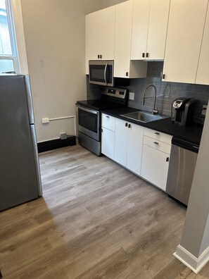 A modern kitchen with stainless steel appliances, white cabinets, and a grey countertop.