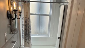 A bathroom with a white sink, toilet, and shower. There is a window with frosted glass and a curtain. - 1880 Yellow-Brick Cottage Executive Retreat (London)