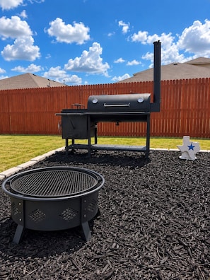 Ein Grill und eine Grillpfanne in einem Garten mit Holzzaun und blauem Himmel.