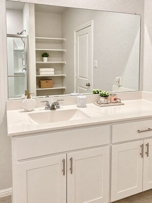 Une salle de bain avec un meuble-lavabo blanc, un grand miroir, une douche et un porte-serviettes.