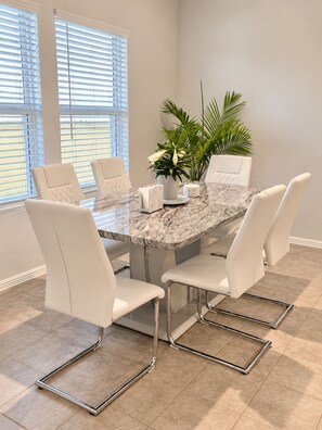 Un coin repas avec une table en marbre, des chaises blanches et une plante en pot.
