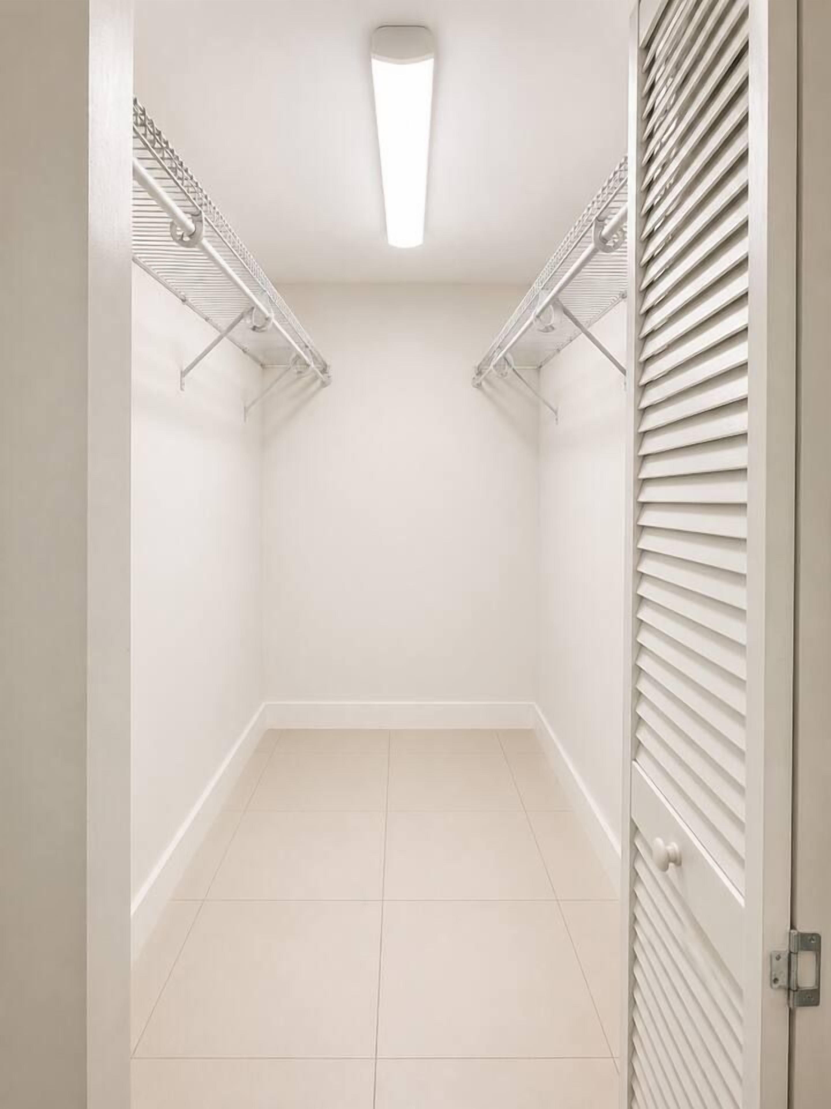 Ein begehbarer Kleiderschrank mit Deckenleuchte, weißen Wänden und Fliesenboden.