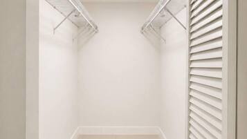 Ein begehbarer Kleiderschrank mit Deckenleuchte, weißen Wänden und Fliesenboden.