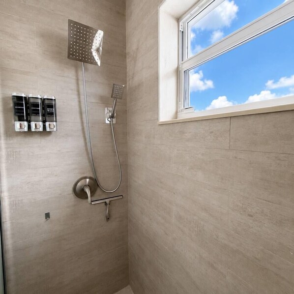 A shower with a handheld showerhead, a wall-mounted rain showerhead, and a window with a view of the sky.