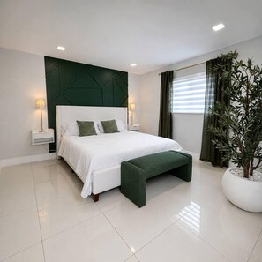 A modern bedroom with a bed, bedside lamps, a green bench, and a potted plant.