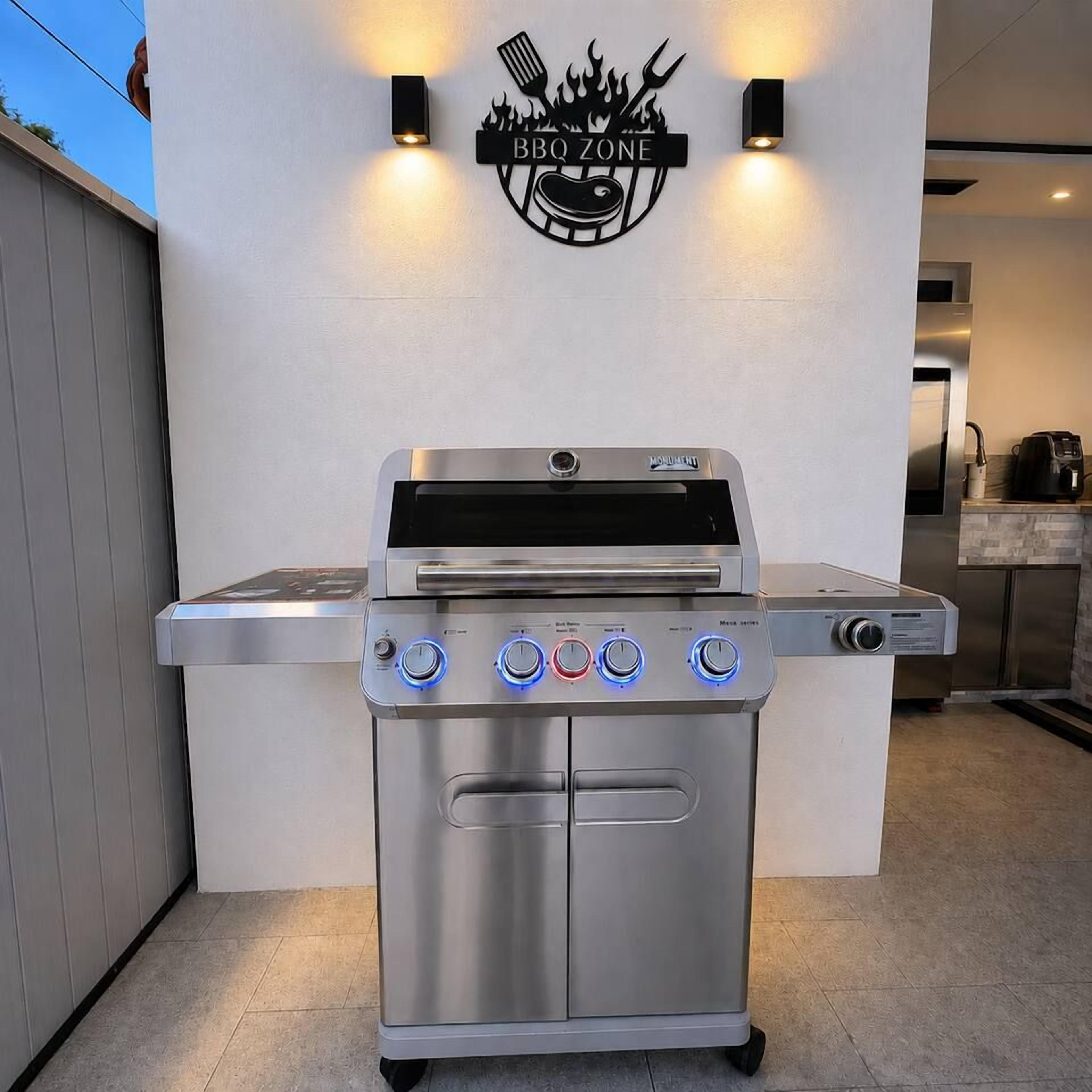 Un barbecue d’extérieur en acier inoxydable, doté d’un écran numérique et de plusieurs boutons de commande, placé devant une enseigne fixée au mur sur laquelle on peut lire « ZONE BARBECUE ».