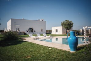 Ein modernes, weißes Gebäude mit Swimmingpool und Liegestühlen.