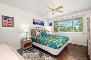 A bedroom with a bed, a nightstand, a ceiling fan, a window with blinds, and a tropical-themed wall art. - Keauhou Palena #604 Kona Retreat With A/C (Kailua-Kona)