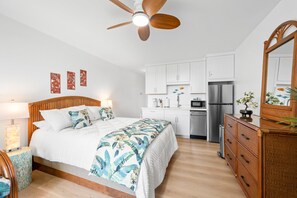 A modern bedroom with a bed, bedside tables, a ceiling fan, and a kitchen area with cabinets and appliances. - Kona Islander Inn#251: Downtown Kona, Remodeled! (Kailua-Kona)