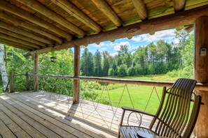 A wooden deck with a swing chair and a view of a forest. - Escape to a Cozy Cabin in the Weston Woods (Weston)
